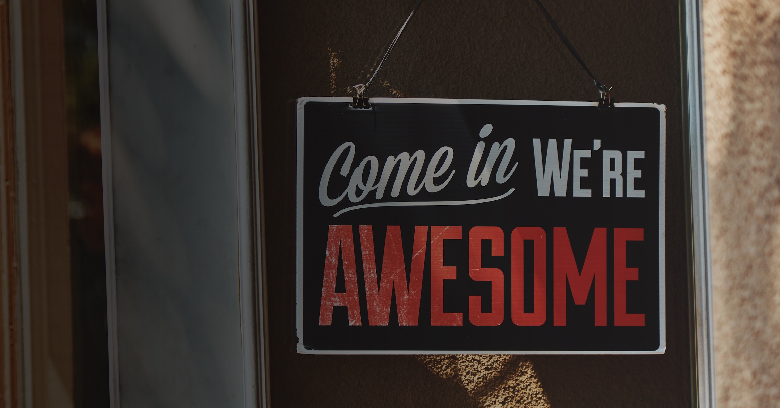 A smiling bank employee in a blue blazer raises her arms in excitement while meeting with a customer in her office.