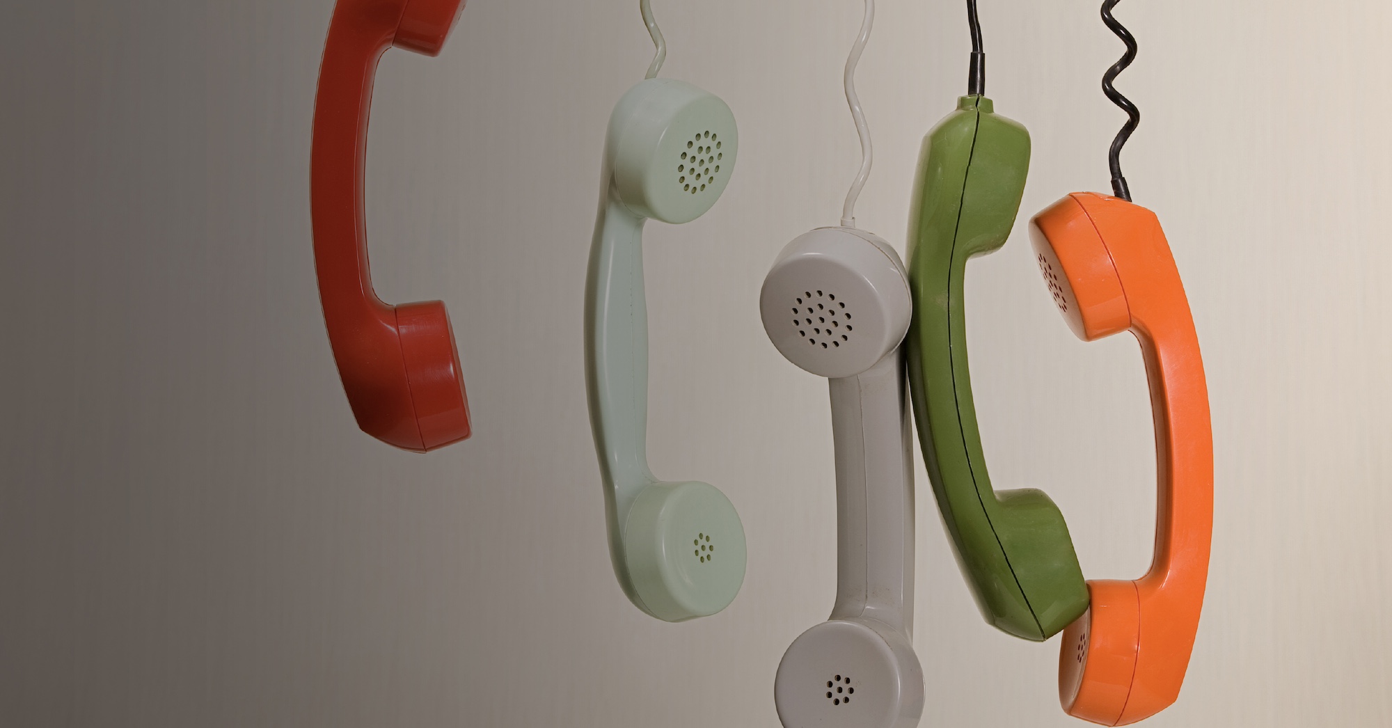 A row of colorful vintage telephone receivers hanging on cords.